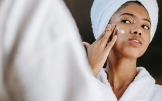 Woman in a robe and towel applying skincare on her cheek