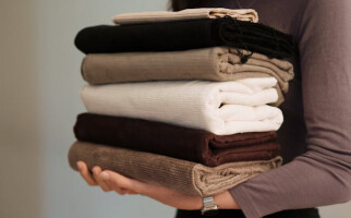 Person holding a pile of various brown and white sweaters