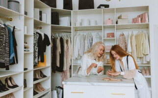 Two women standing in their closet full of clothing, bags, and shoes