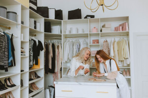Two women standing in a closet full of clothing and accessories